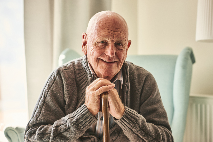 Happy senior man in a sweater with hands crossed over a cane